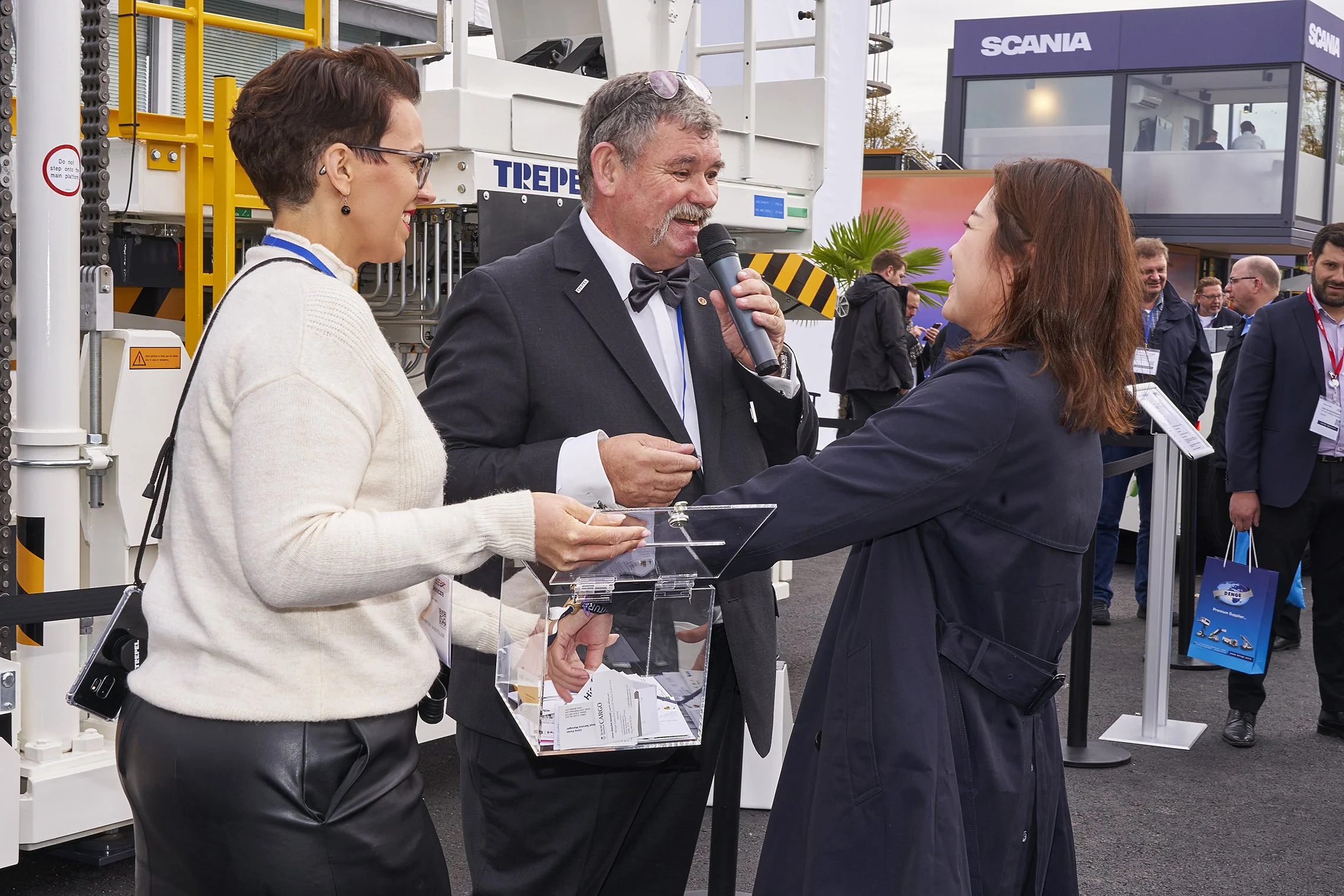 Three people drawing raffle tickets at the TREPEL outdoor stand, one speaking into a microphone