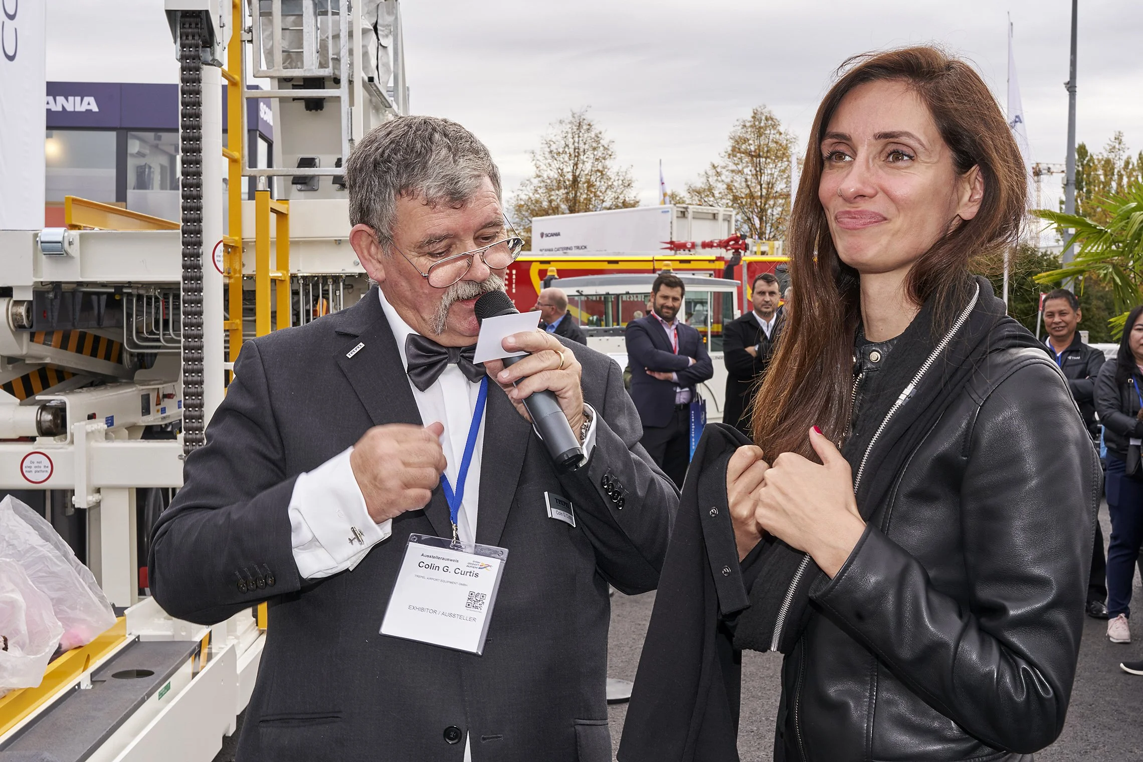 Man with microphone speaking next to a woman at the TREPEL booth during an outdoor event
