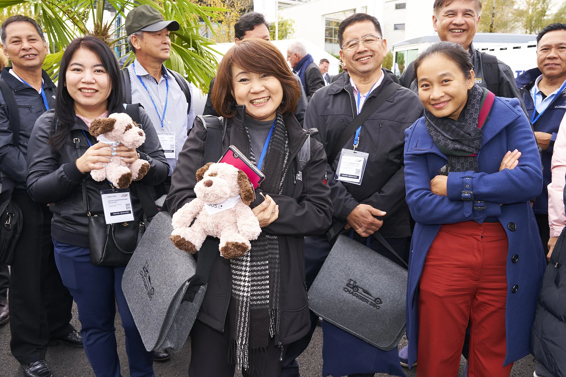 Smiling visitors with plush toys and TREPEL bags posing for a group photo outdoors
