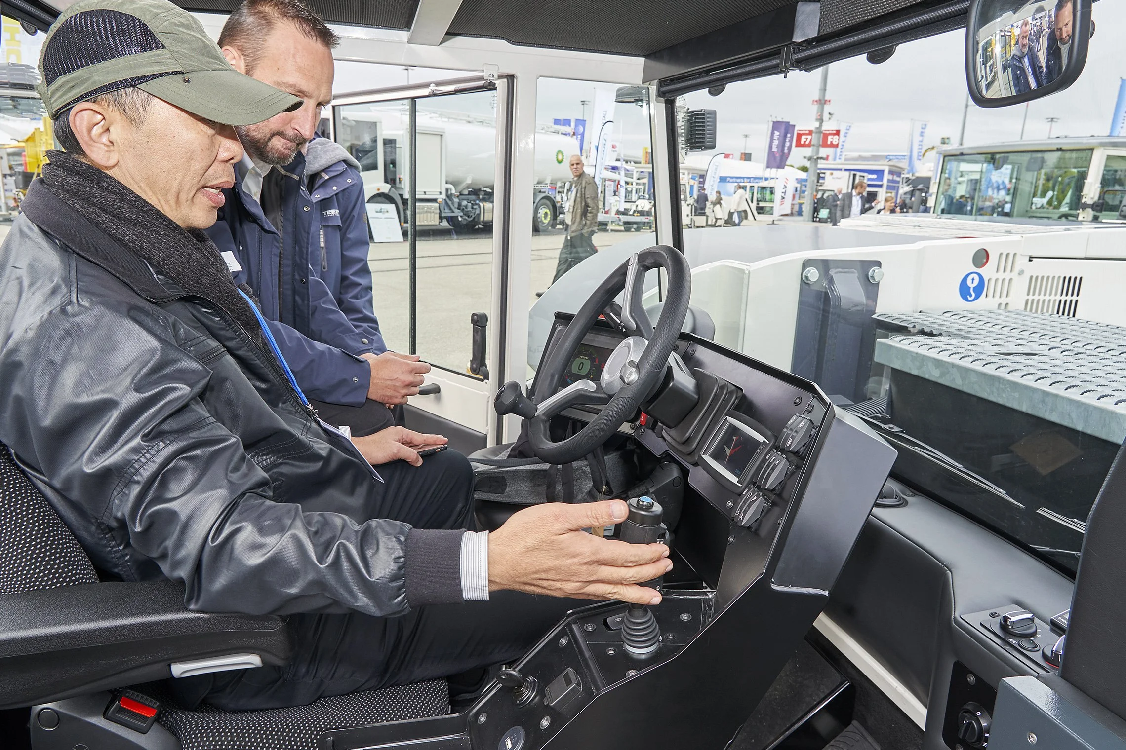 Visitor testing the control unit of a TREPEL tow tractor under supervision at a trade fair