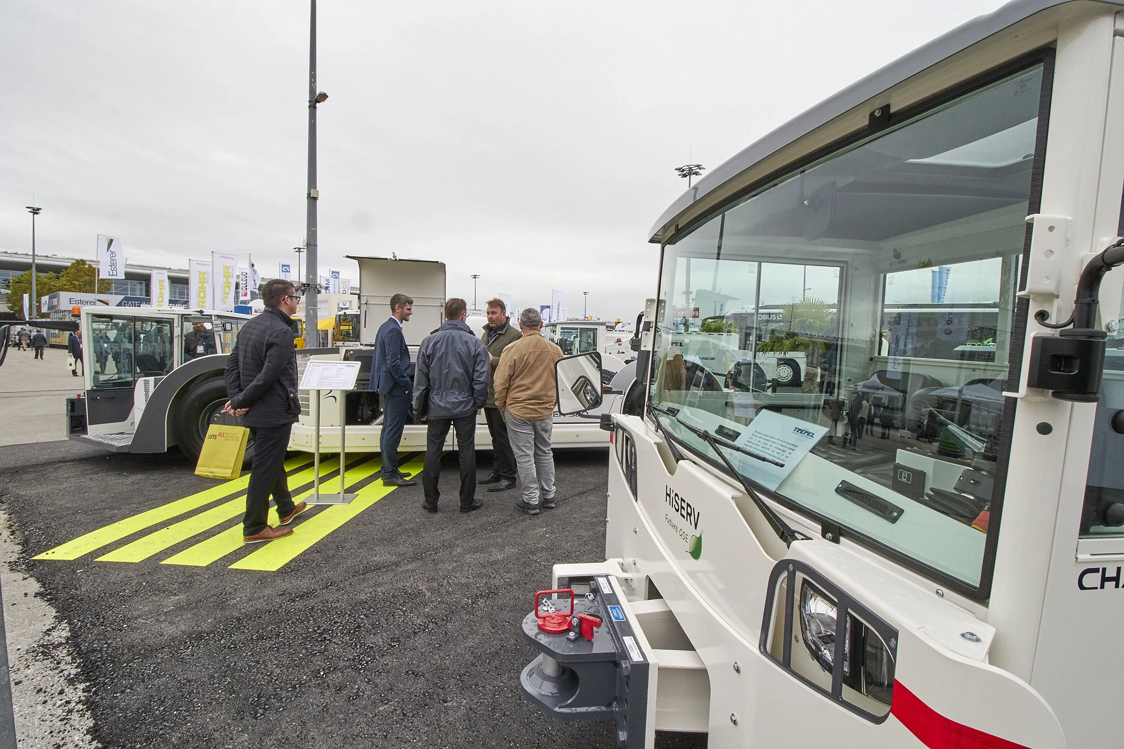 Group of people discussing near TREPEL aircraft tow tractors at an outdoor exhibition booth