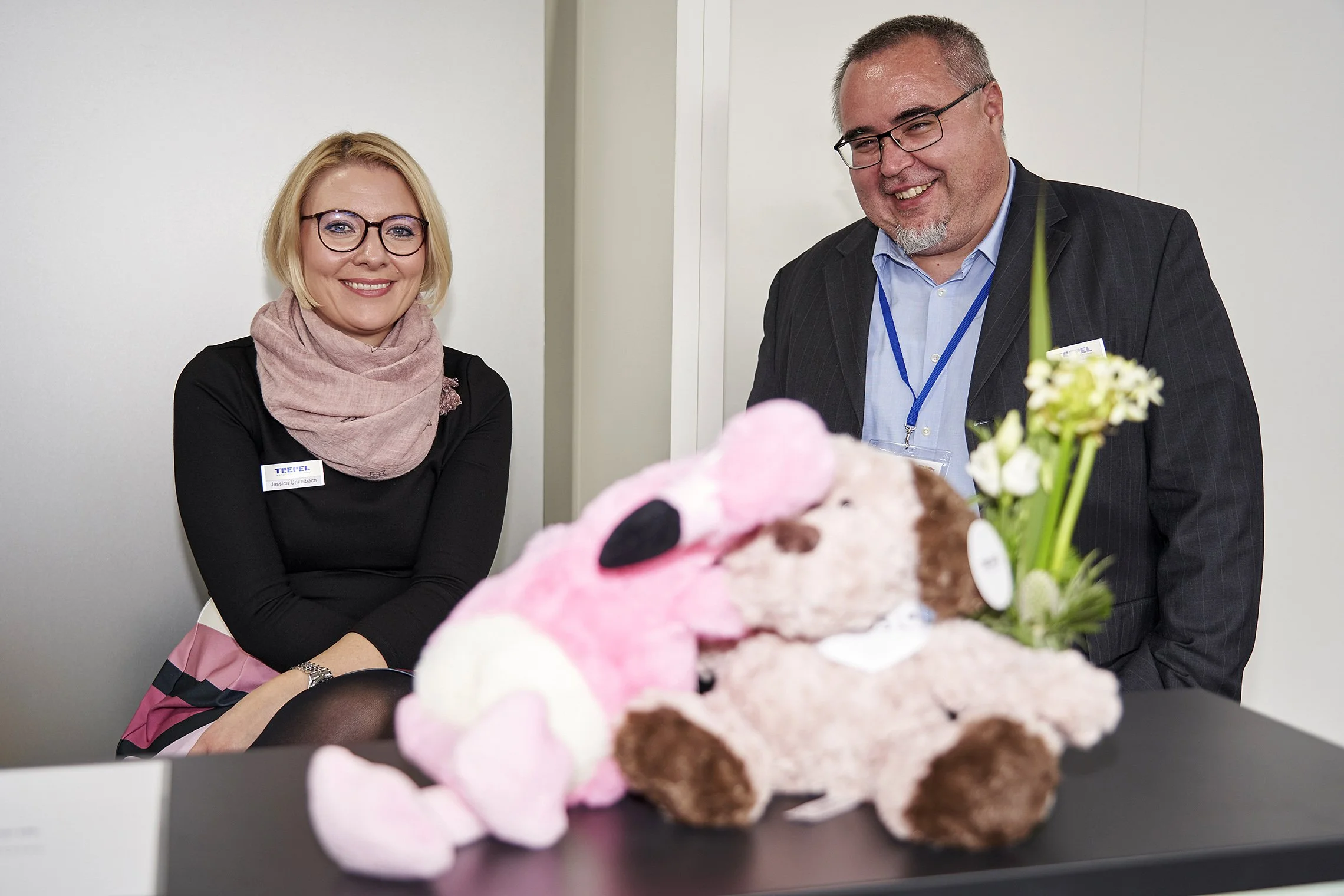 Woman and man smiling behind a counter with stuffed animals and a flower at the TREPEL booth