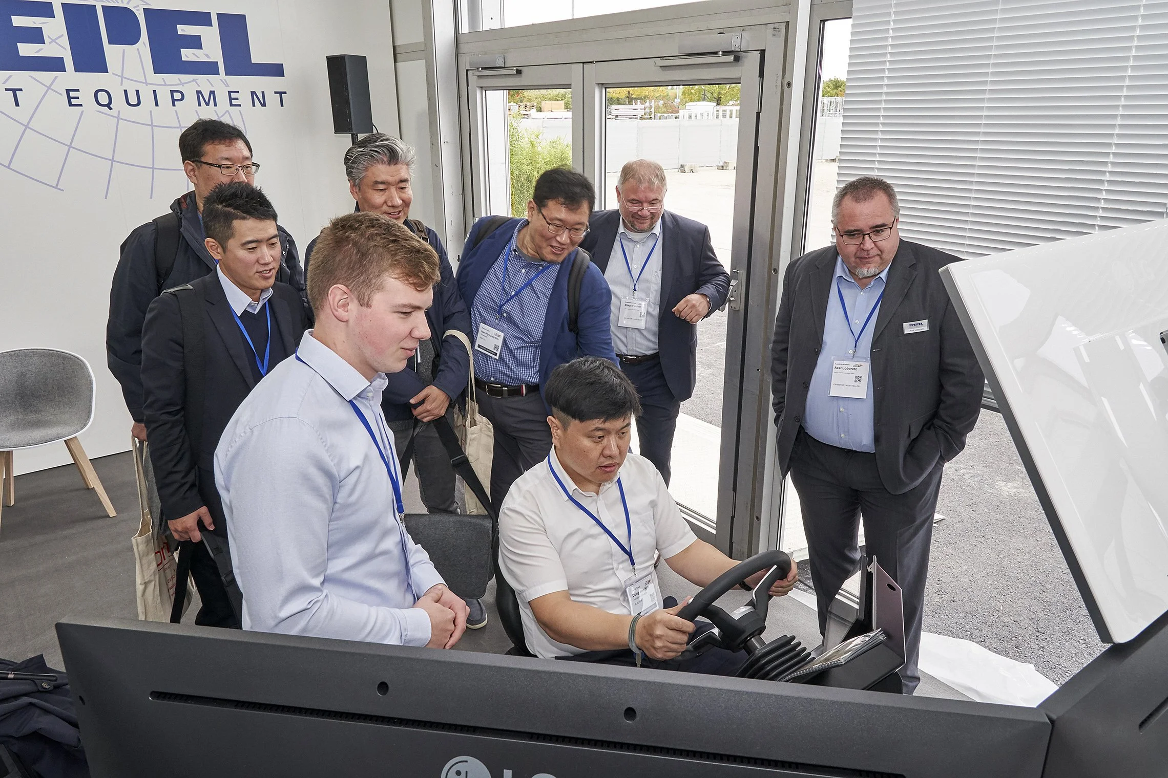 Group of visitors gathered around a TREPEL driving simulator during a demonstration
