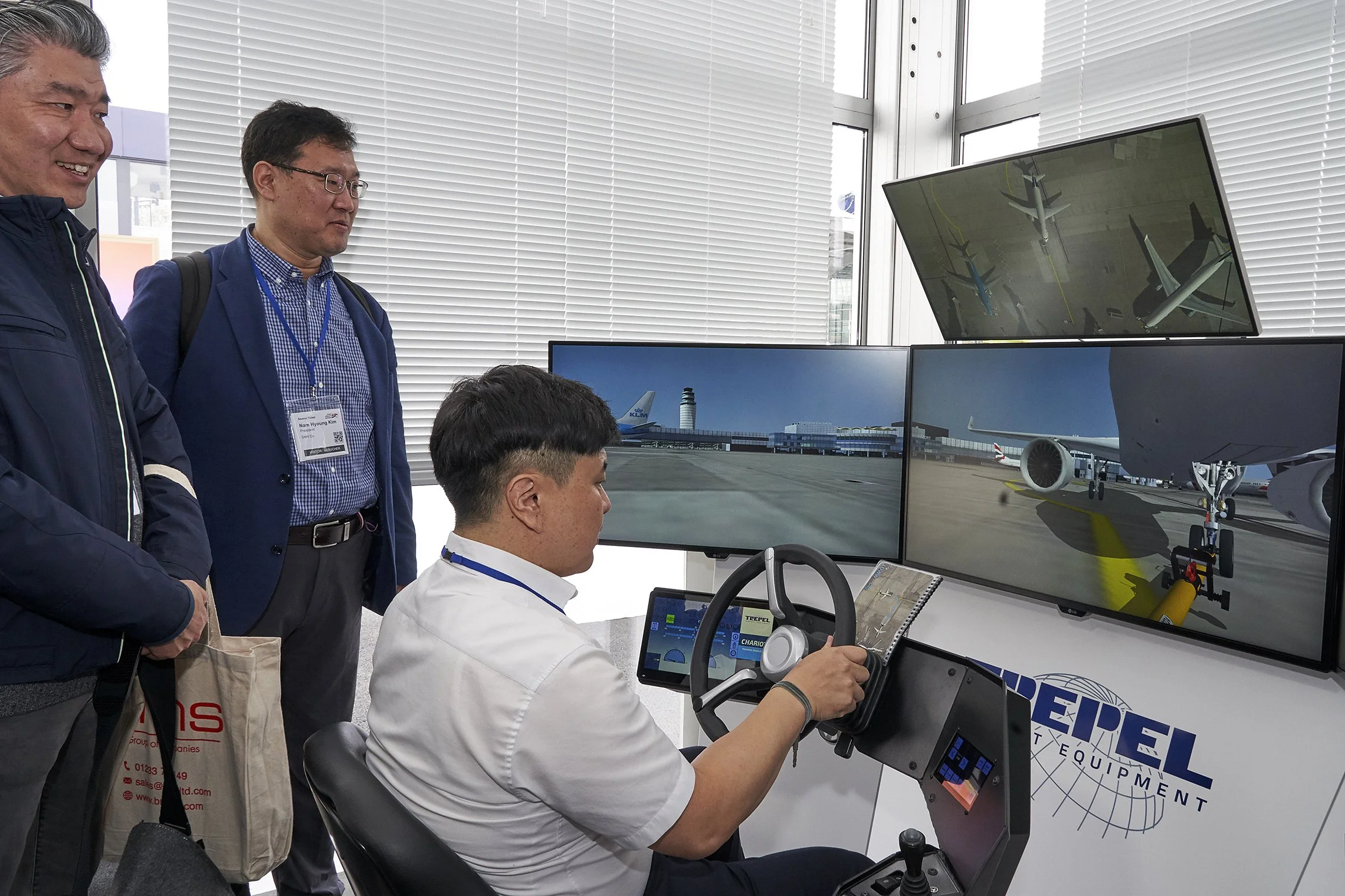 Man testing a TREPEL ground support simulator with multiple screens while two visitors observe