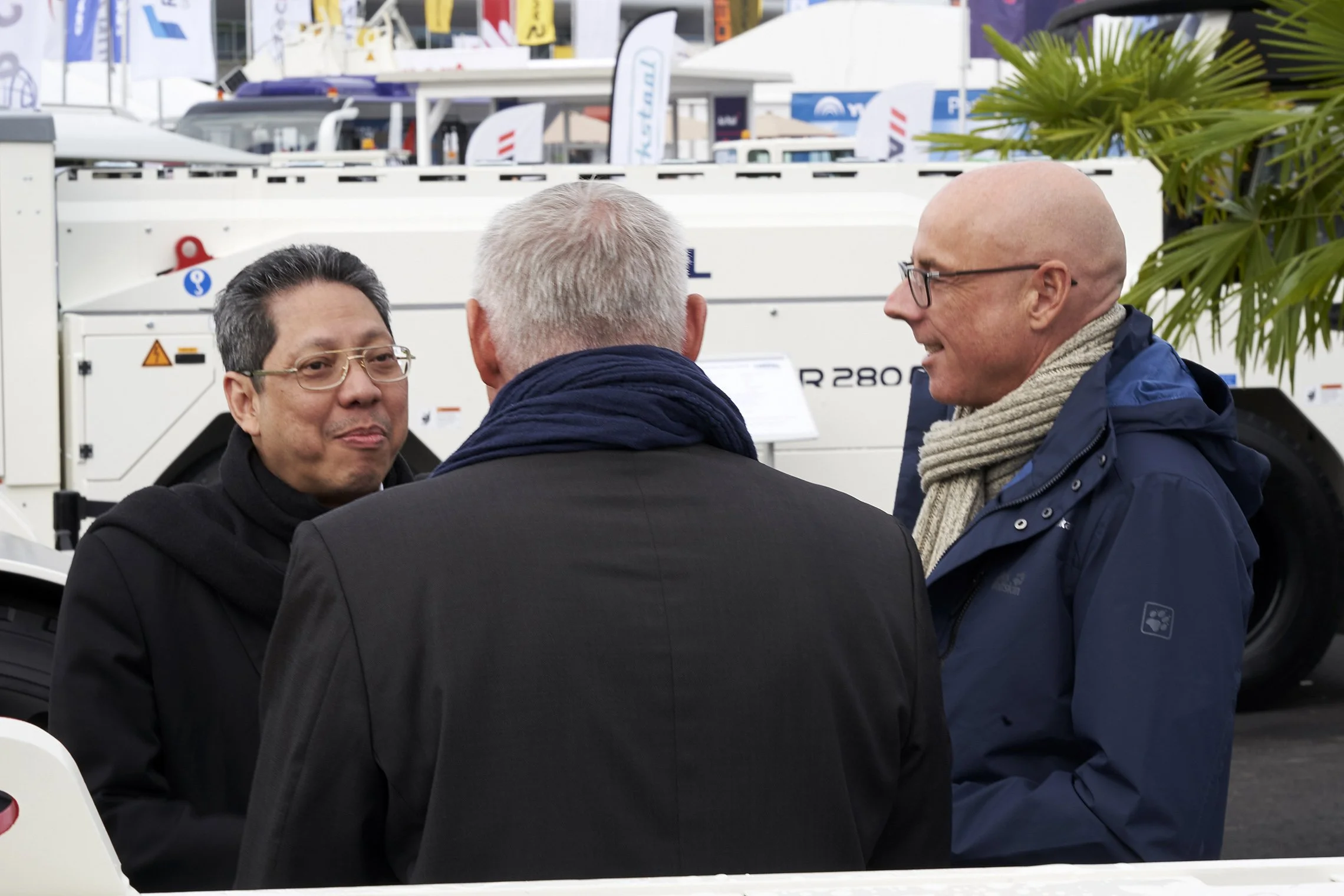 Three people in conversation in front of a TREPEL aircraft tractor at an outdoor exhibition