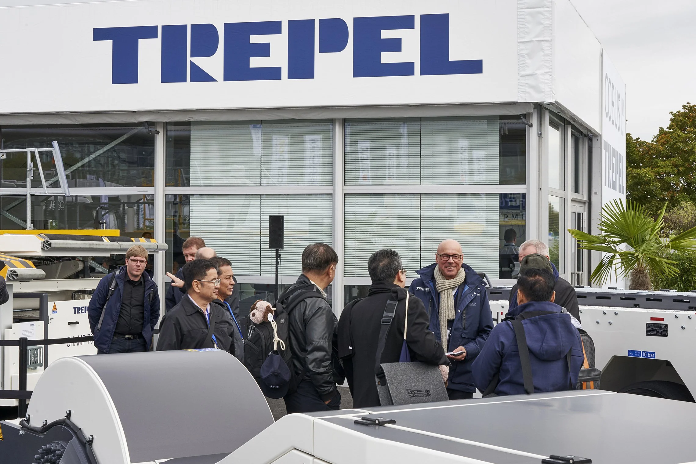 Group of international visitors gathered in front of the TREPEL booth building during a tour