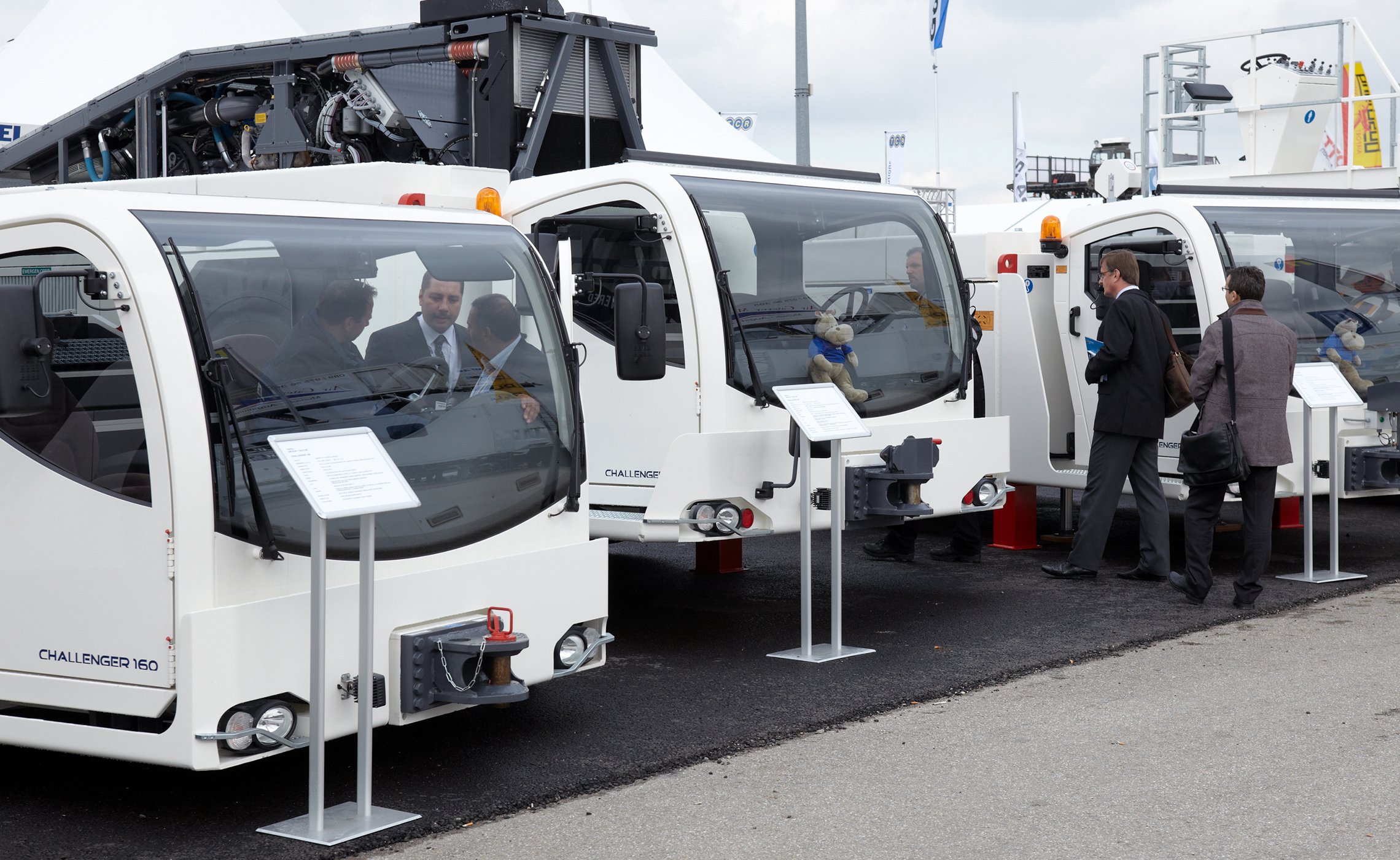 Drei CHALLENGER-Schlepper von TREPEL nebeneinander auf einer Messe ausgestellt, mit Besuchern und Infotafeln davor