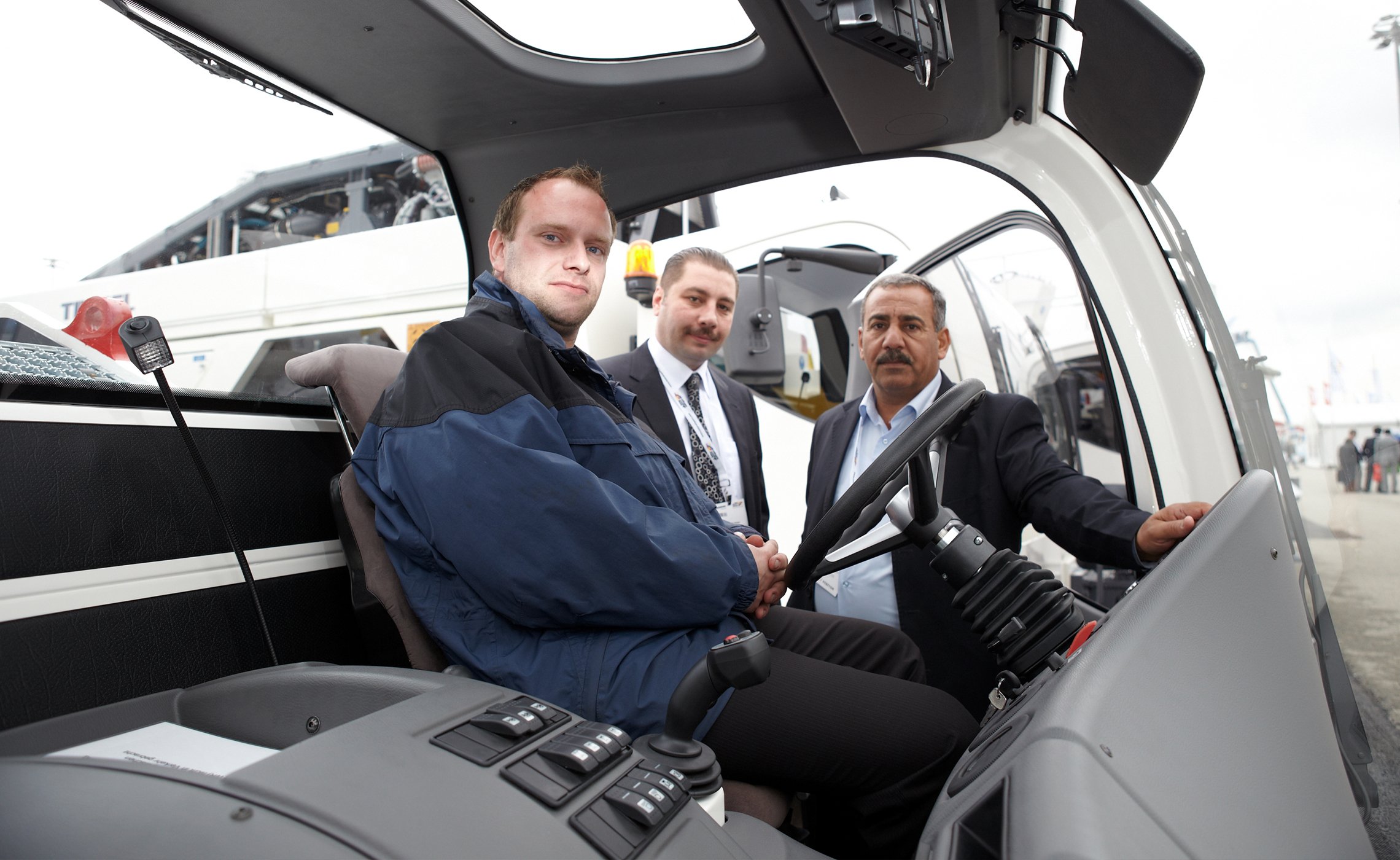 Das Bild zeigt die Innenansicht der Fahrerkabine eines TREPEL-Schleppers. Ein Mann sitzt auf dem Fahrersitz und betrachtet die Kamera, während zwei weitere Männer draußen am Fahrzeug stehen und in das Cockpit schauen. Die Szene wirkt wie ein technisches Beratungsgespräch während einer Produktvorführung auf der Messe.