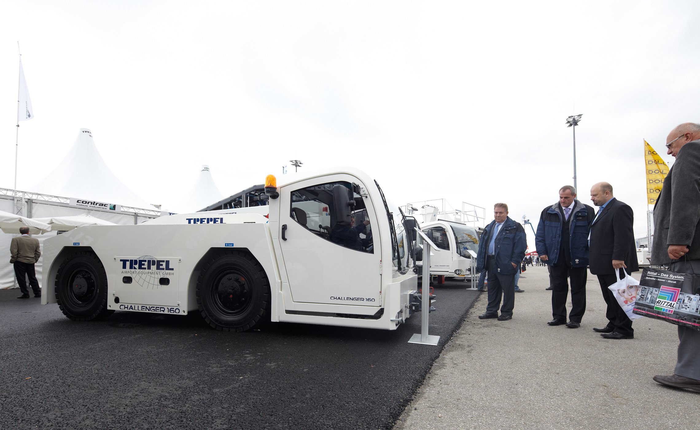 Männergruppe betrachtet ein ausgestelltes CHALLENGER 160 Flugzeugschleppfahrzeug von TREPEL auf dem Messegelände