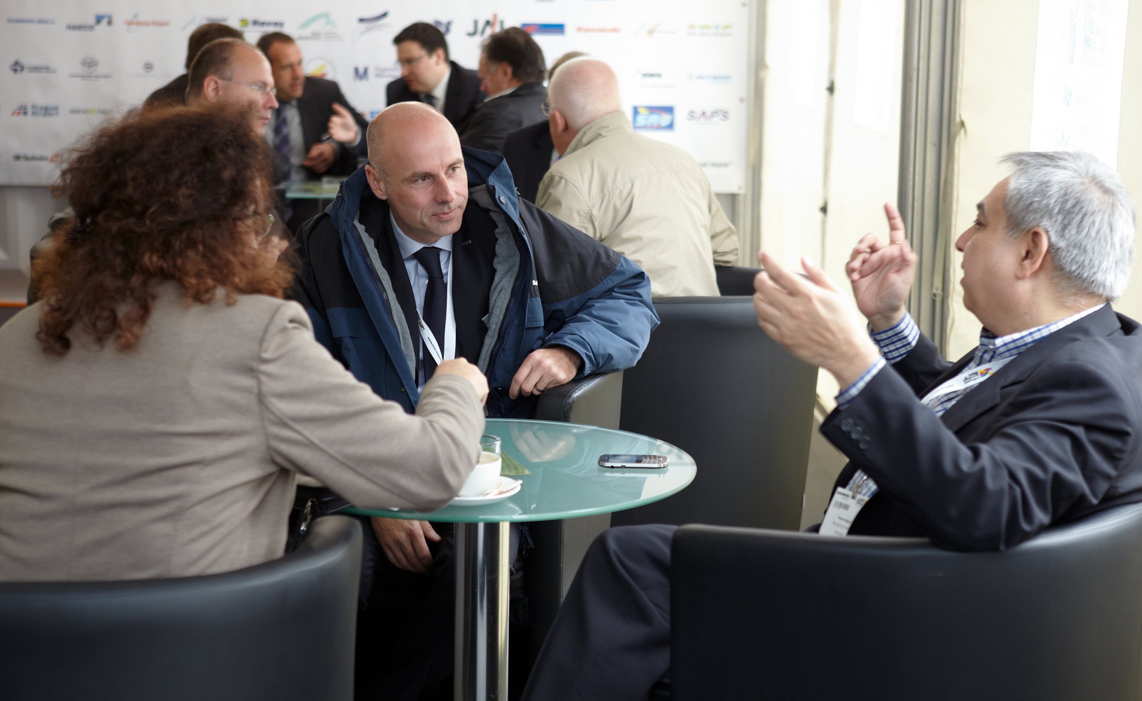 Drei Personen im Gespräch an einem runden Glastisch im TREPEL-Messezelt während der Inter Airport Europe