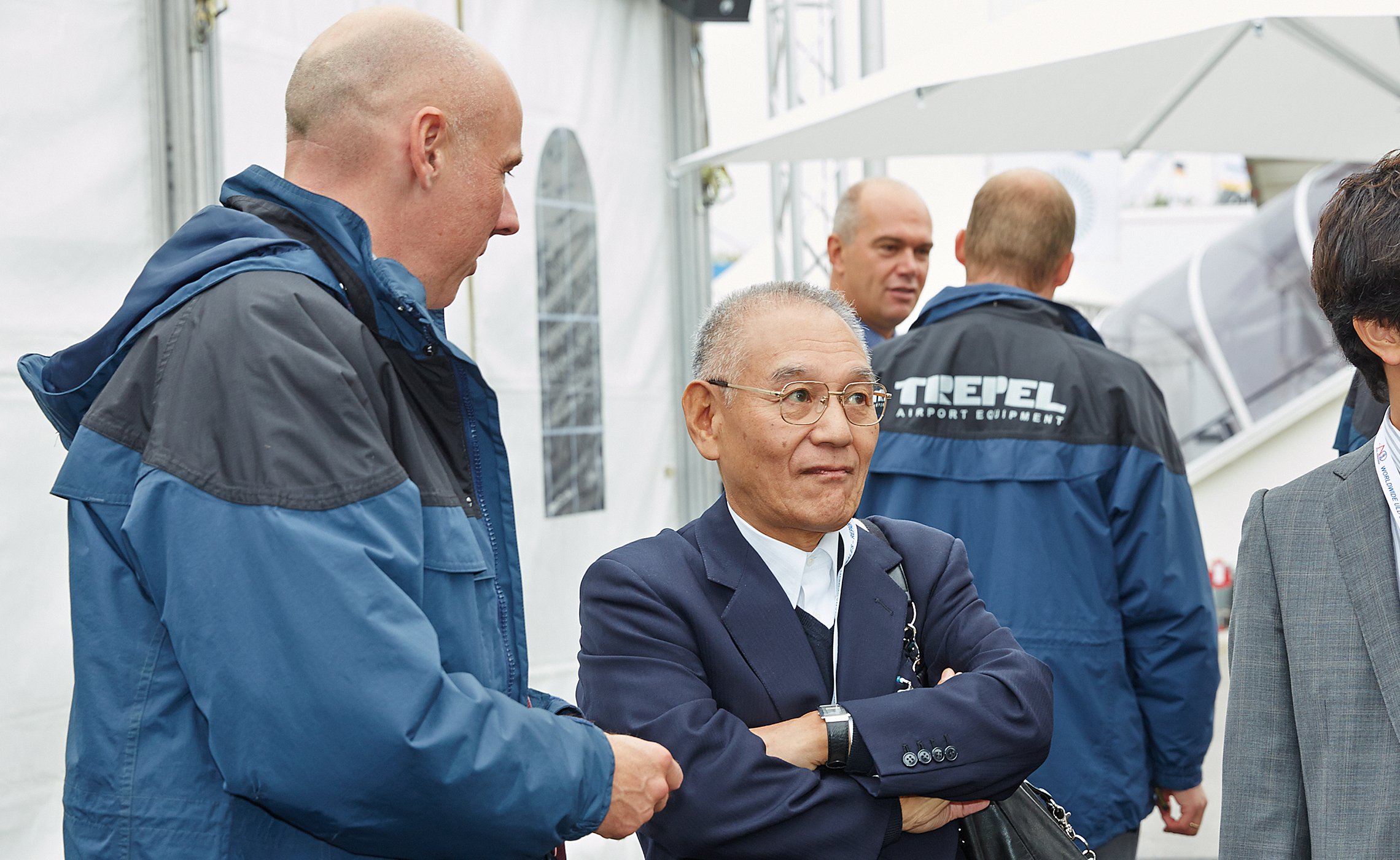 Zwei Männer im Gespräch, im Hintergrund TREPEL-Mitarbeiter mit Jacken mit Firmenlogo