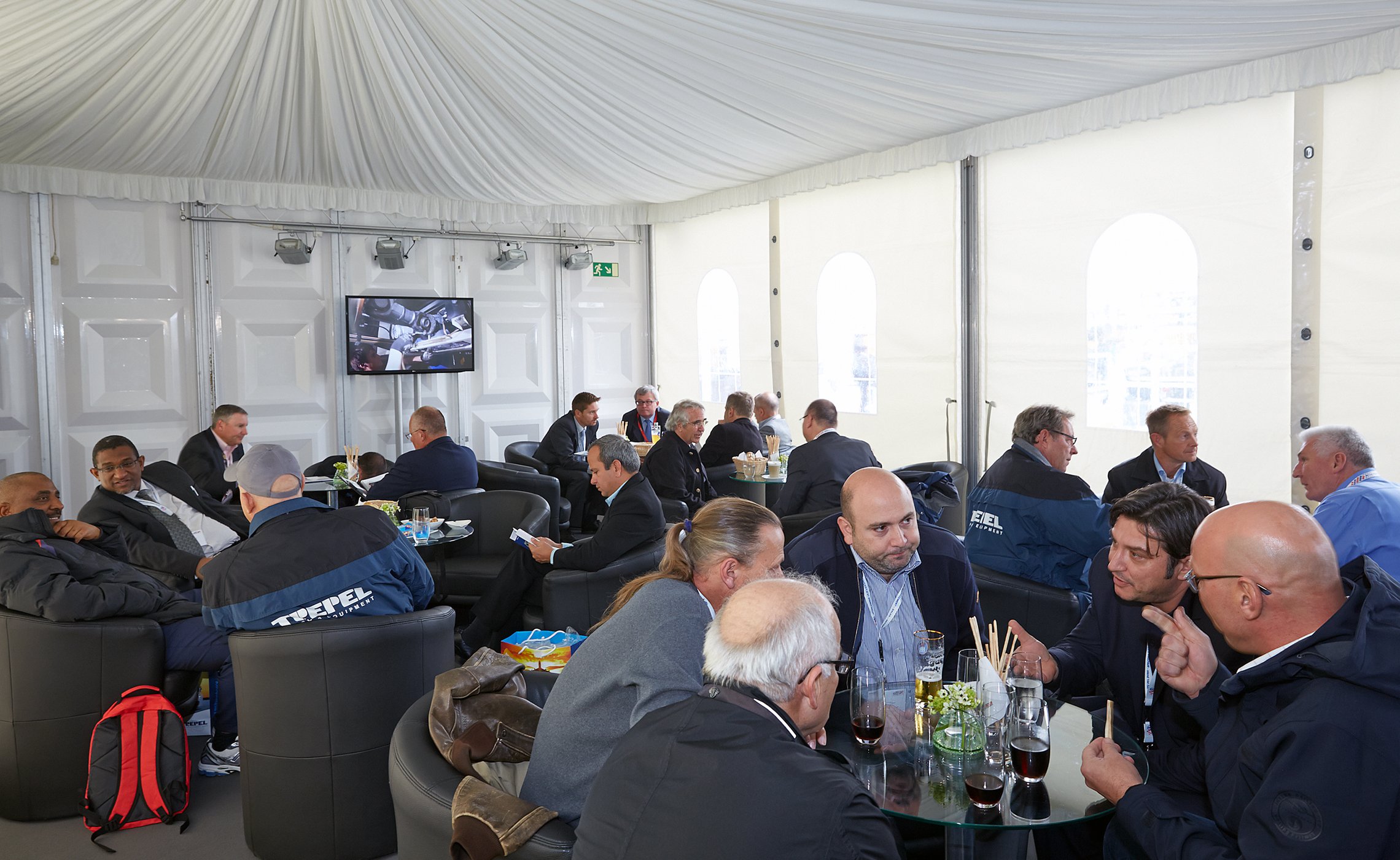 Messebesucher sitzen an Tischen im Zelt und führen Gespräche, TREPEL-Jacken erkennbar