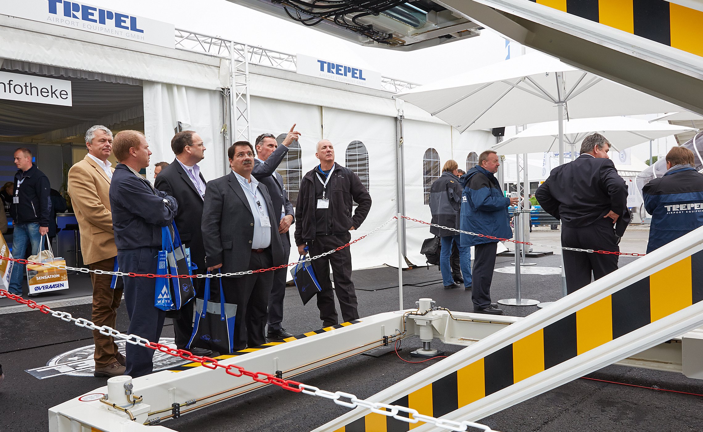 Besuchergruppe beobachtet aufmerksam ein Hebefahrzeug am TREPEL-Stand auf einer Messe