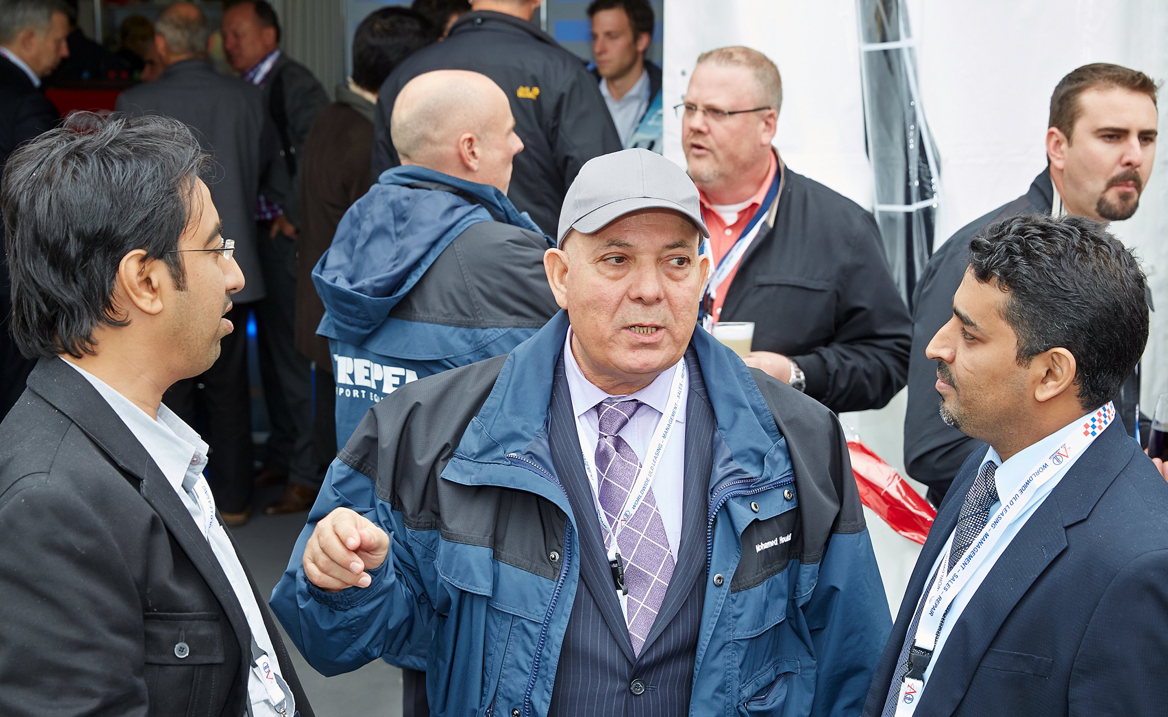 Eine Gruppe von Männern im Anzug und mit Namensschildern führt ein angeregtes Gespräch vor dem Messestand von TREPEL