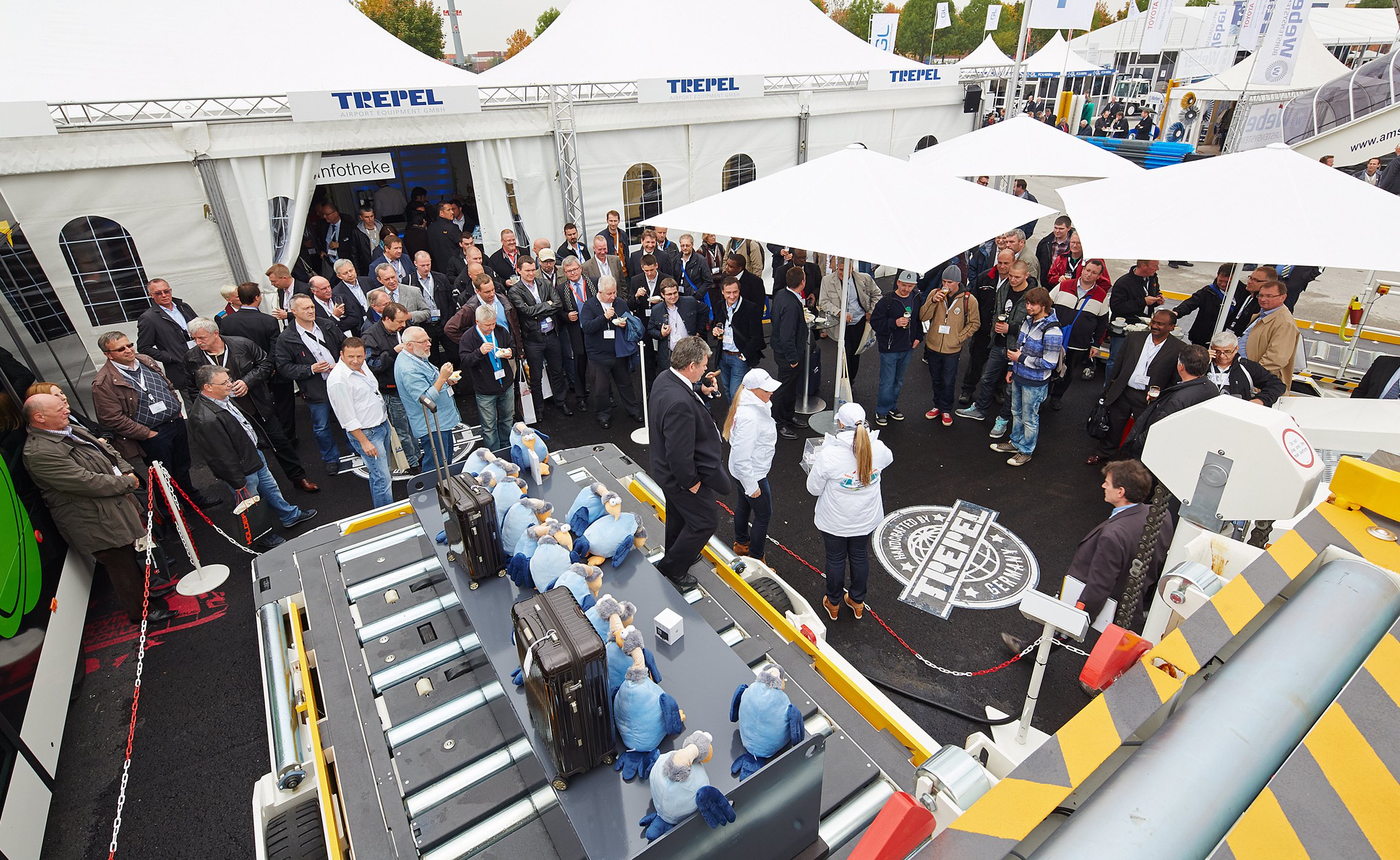 Zahlreiche Messebesucher stehen vor dem TREPEL Stand und verfolgen eine Vorführung mit einem Förderfahrzeug und Gepäckstücken