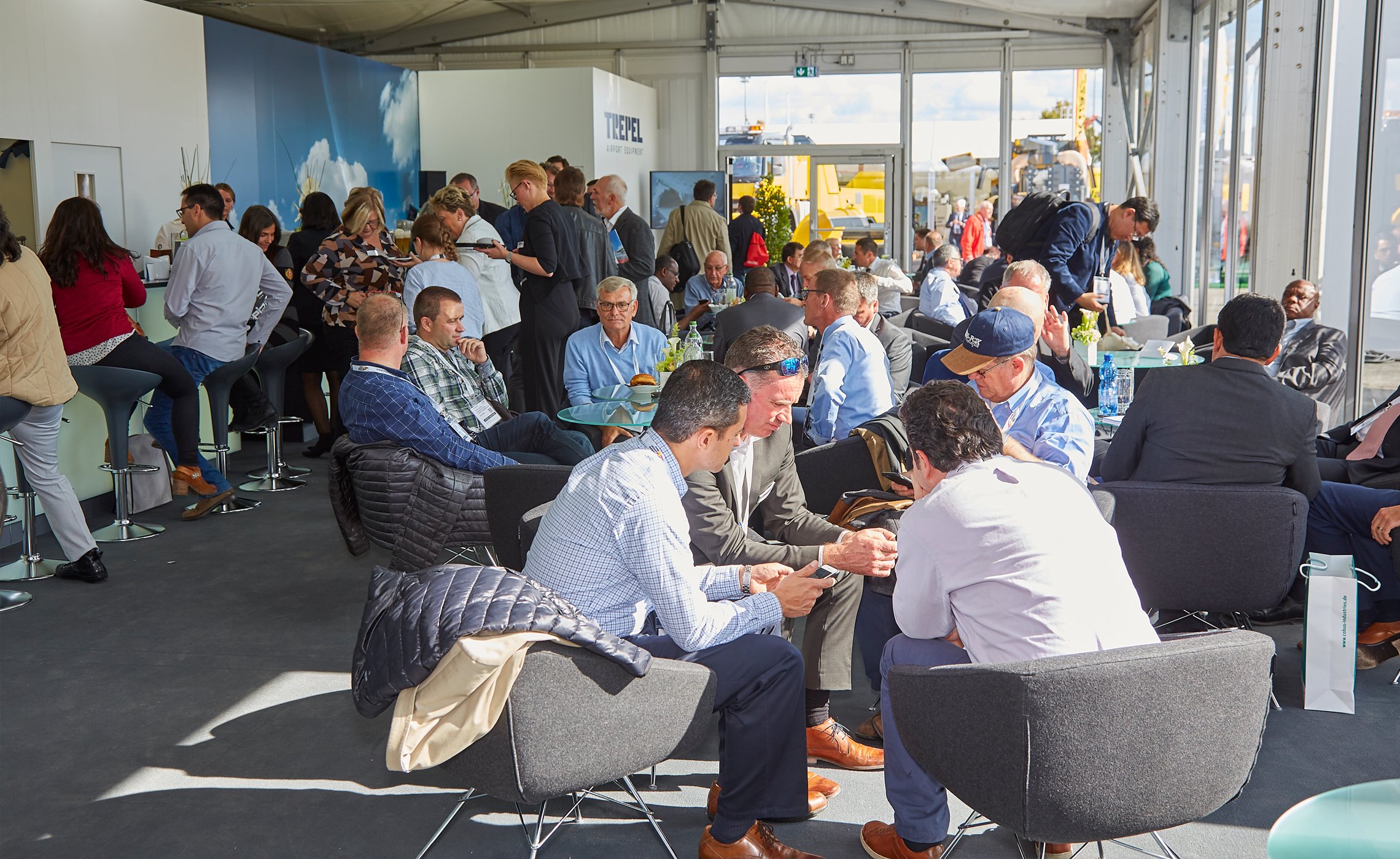 Trade fair visitors in conversation at the TREPEL indoor lounge with natural light and relaxed seating