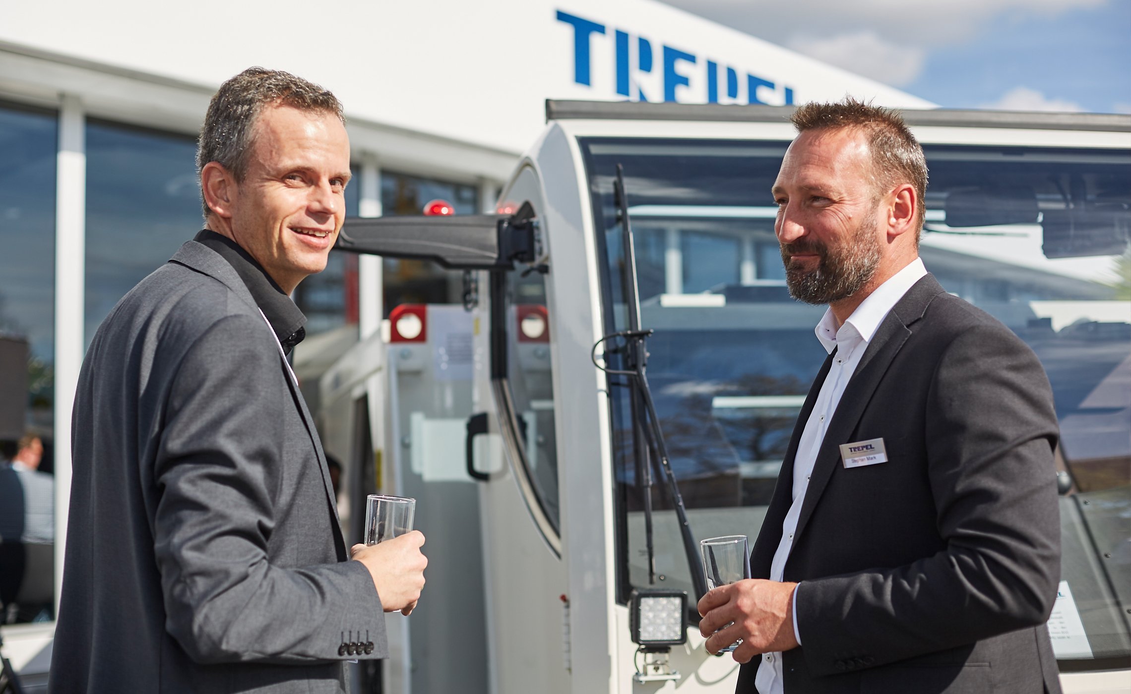 Zwei Männer im Gespräch mit Getränkegläsern vor einem Fahrzeug am TREPEL-Messestand
