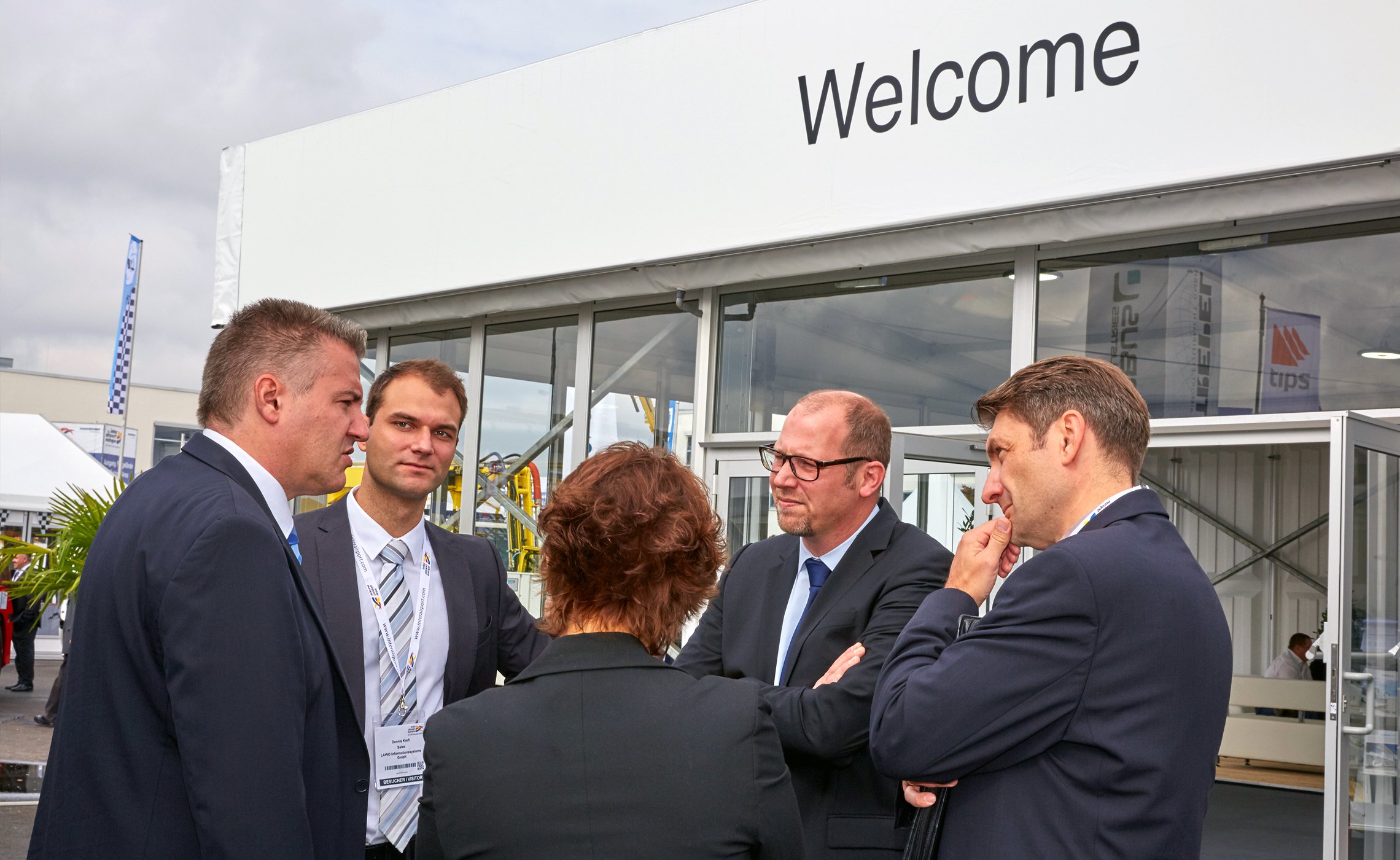 Fünf Personen im Business-Outfit im Gespräch vor dem Eingang des TREPEL-Messezelts mit „Welcome“-Schriftzug