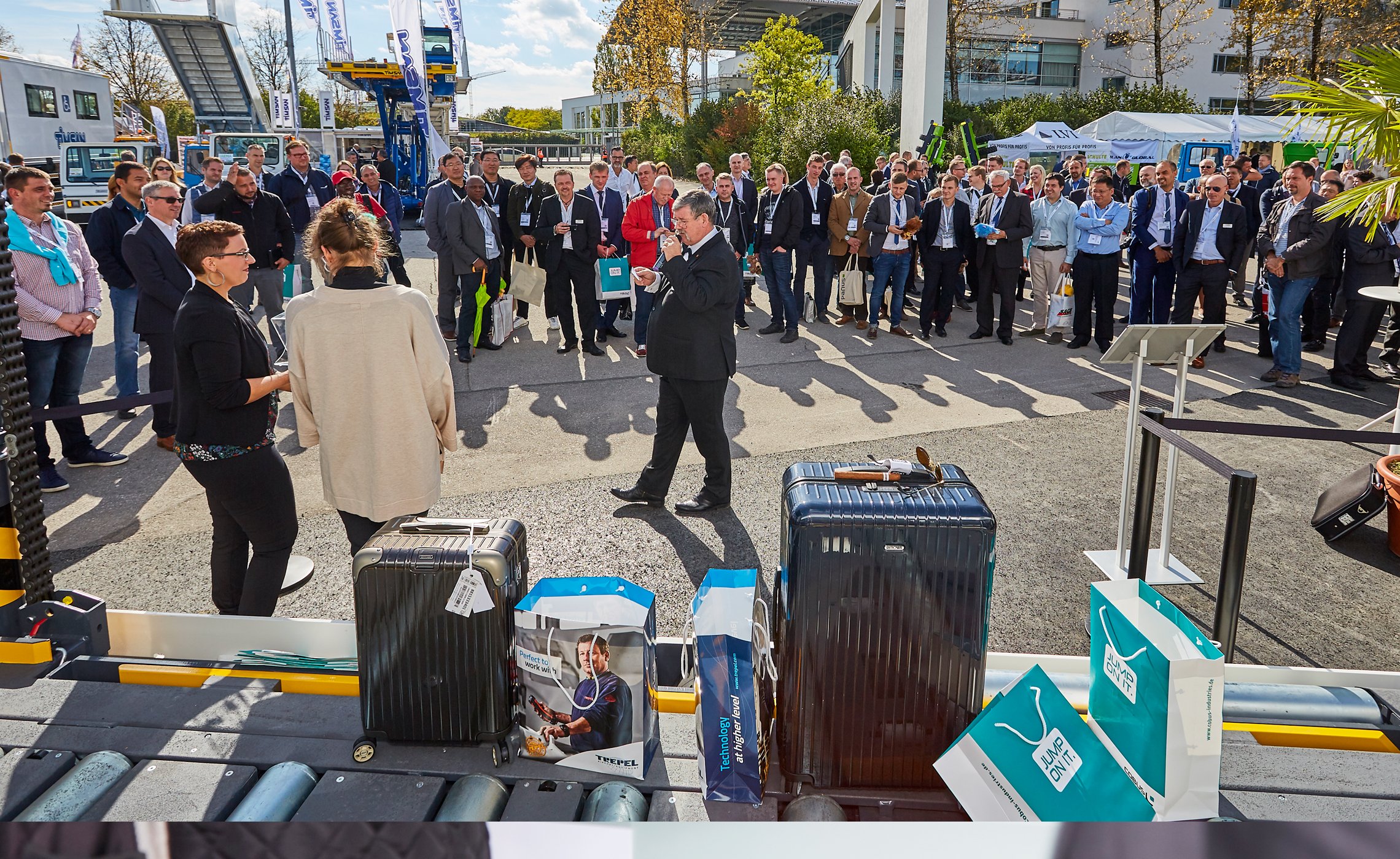 Menschenmenge bei einer Verlosung auf dem Außengelände der Inter Airport Europe Messe mit Moderator, Koffern und Werbegeschenken