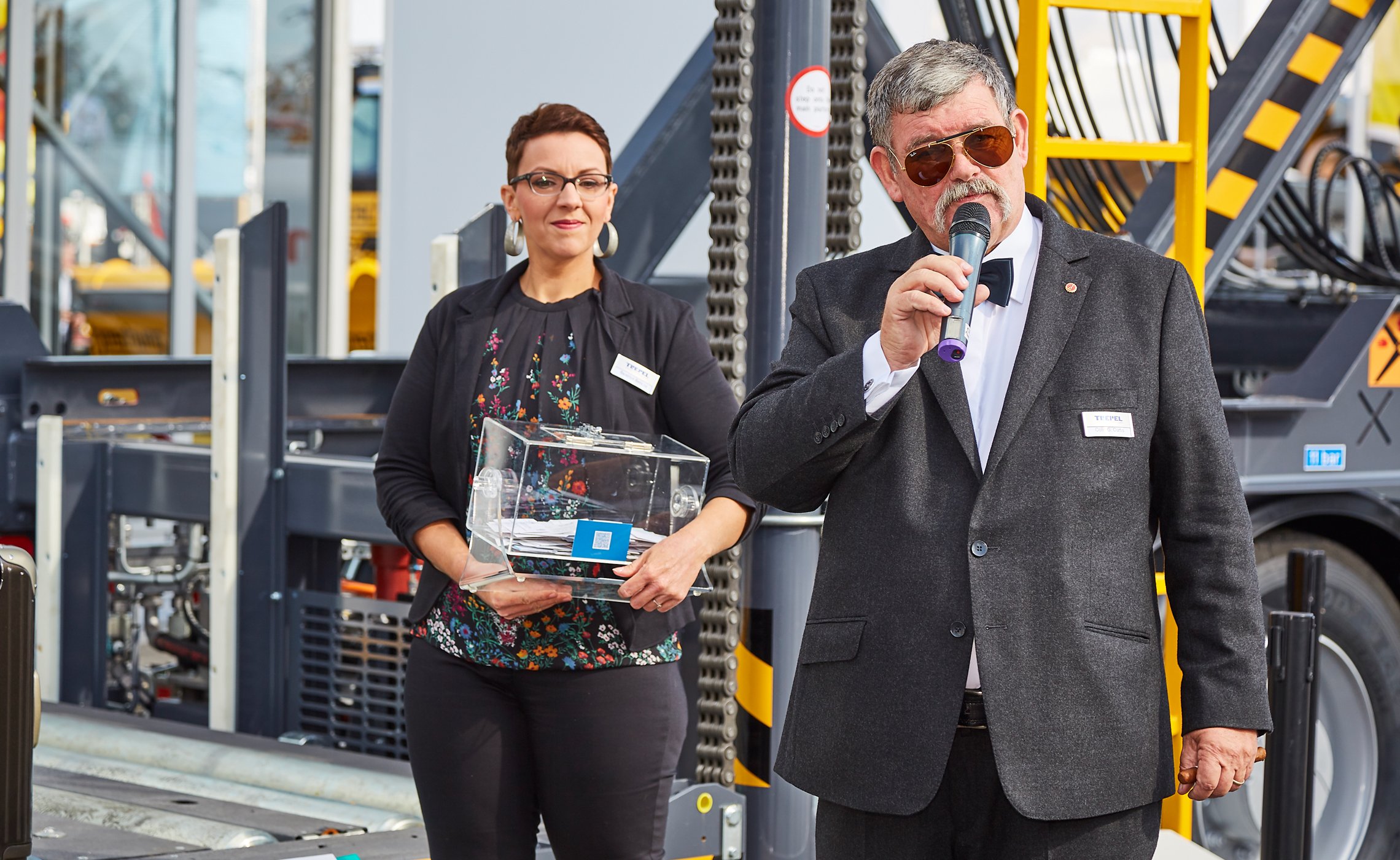 Mann mit Mikrofon moderiert Verlosung, daneben eine Frau mit Lostrommel