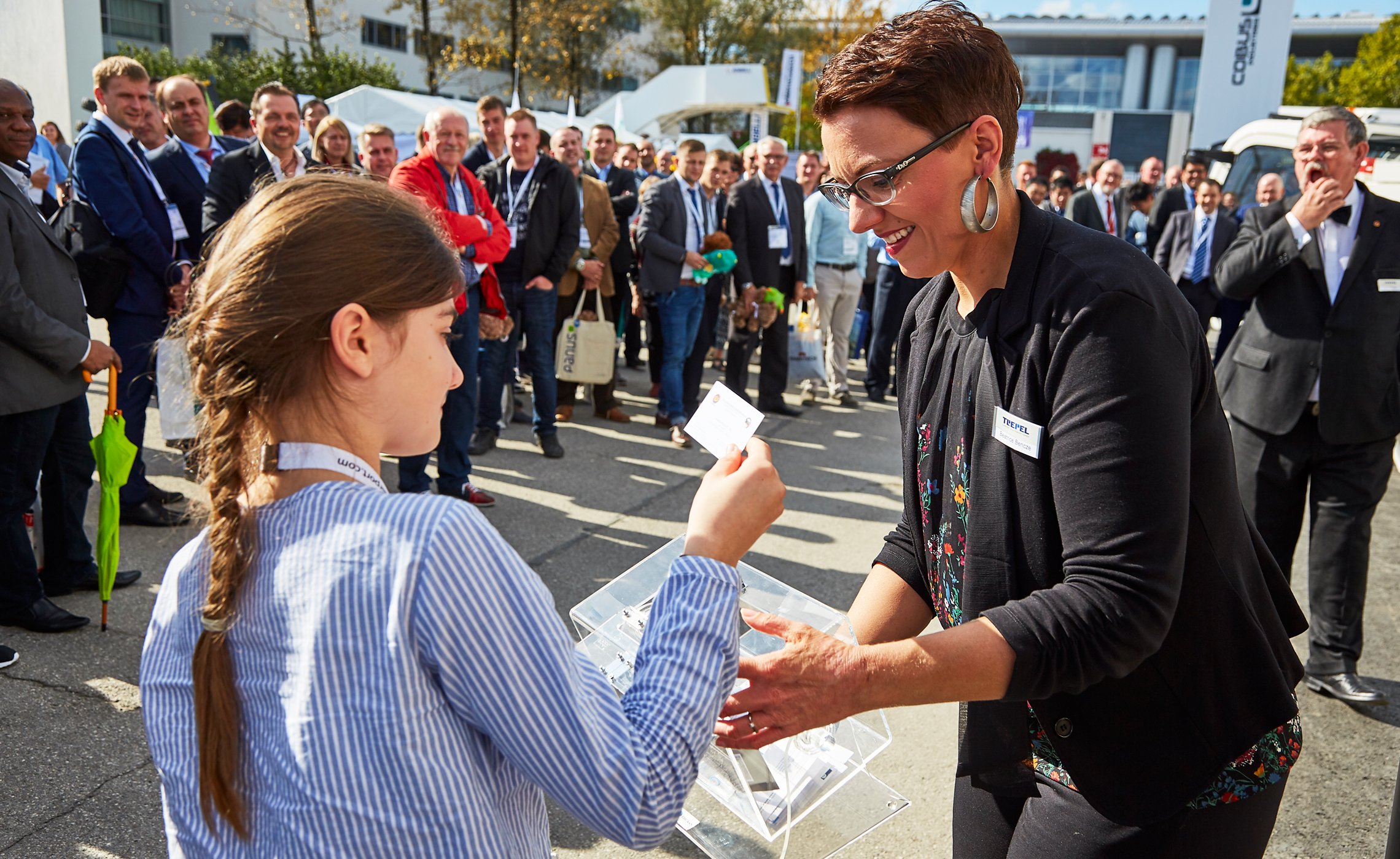 Mädchen zieht Los aus einer Box, daneben eine lächelnde TREPEL-Mitarbeiterin