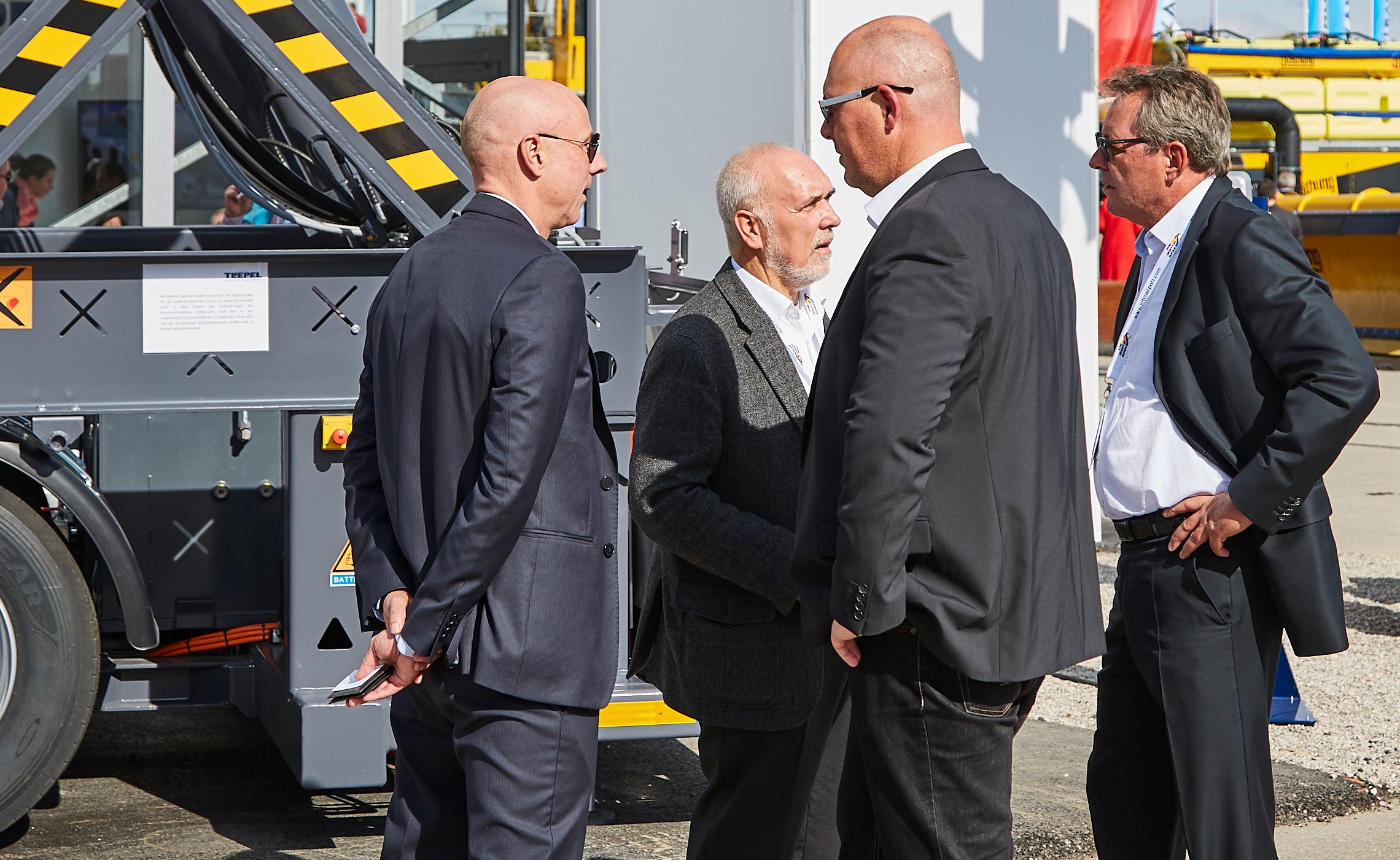 Vier Männer im Anzug diskutieren vor einem TREPEL Flughafenfahrzeug
