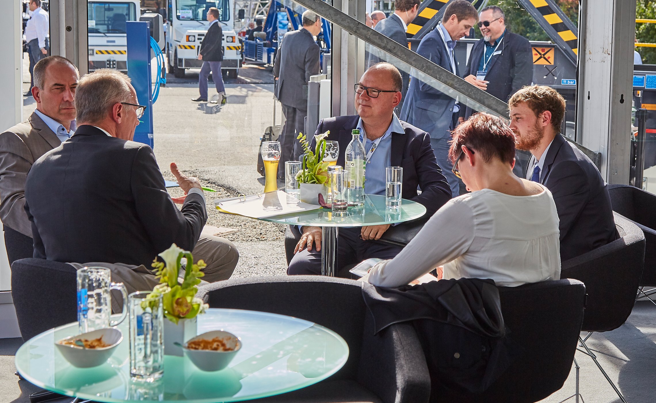 Fünf Personen in Businesskleidung sitzen an einem runden Tisch in einem Messezelt